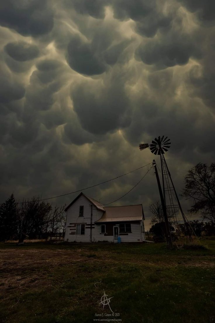 a white house sitting under a cloudy sky next to a windmill