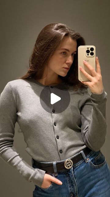 a woman taking a selfie with her cell phone while wearing jeans and a cardigan sweater