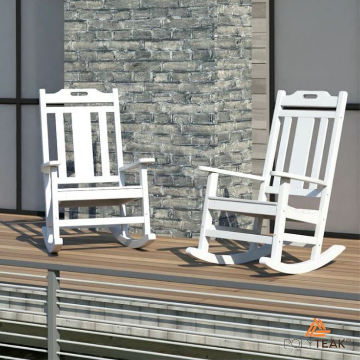 two white rocking chairs sitting next to each other on a wooden deck in front of a brick wall