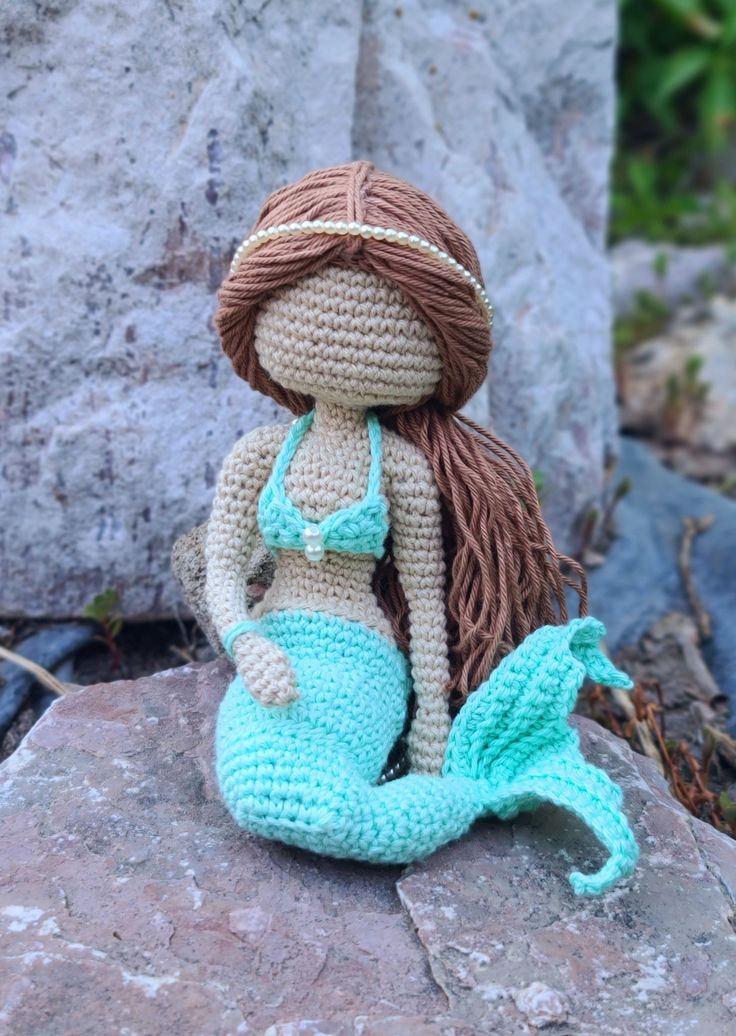 a crocheted mermaid doll sitting on top of a rock