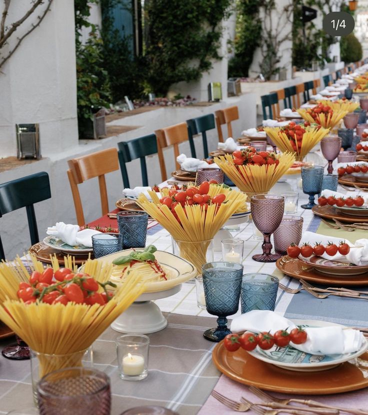 a long table is set with plates, glasses and strawberries in vases on it