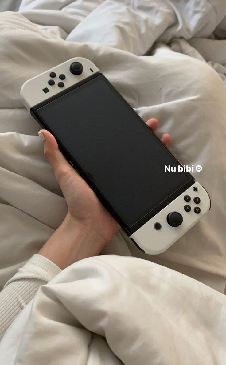 a person holding a nintendo wii game controller in their hand on top of a bed