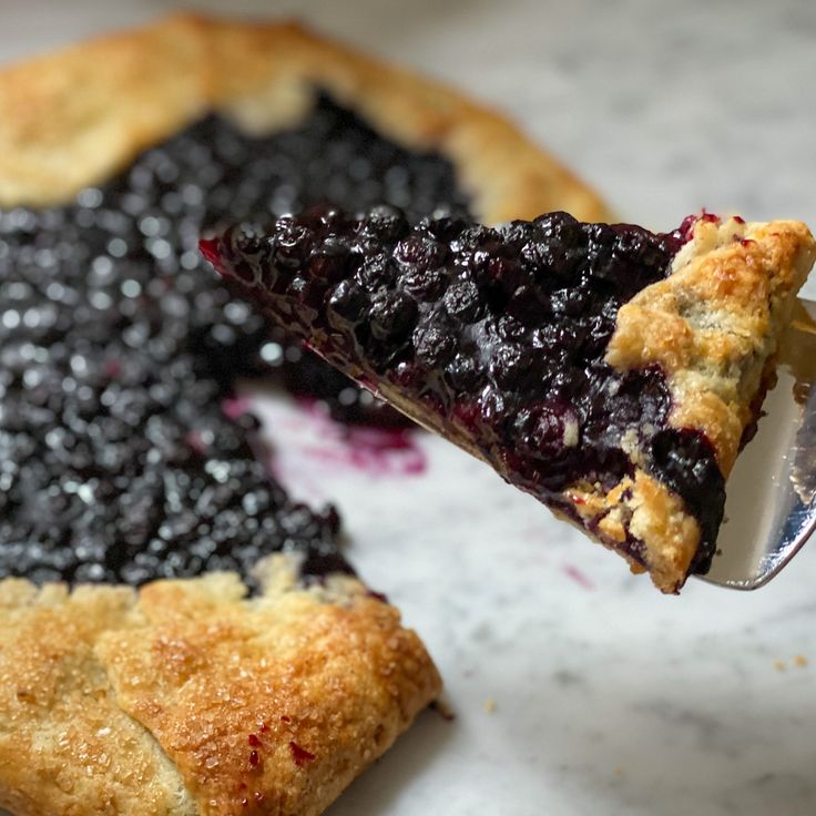 a slice of blueberry pie being held by a fork with a bite taken out