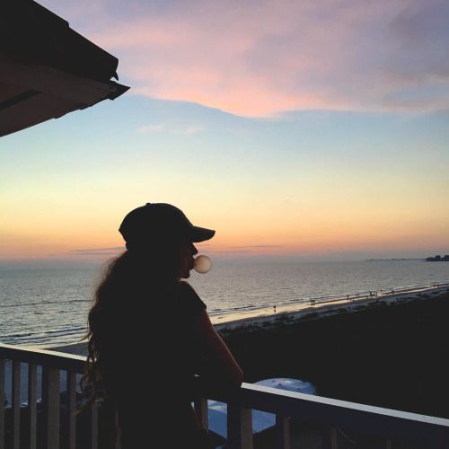 a woman standing on top of a balcony next to the ocean at sunset or dawn