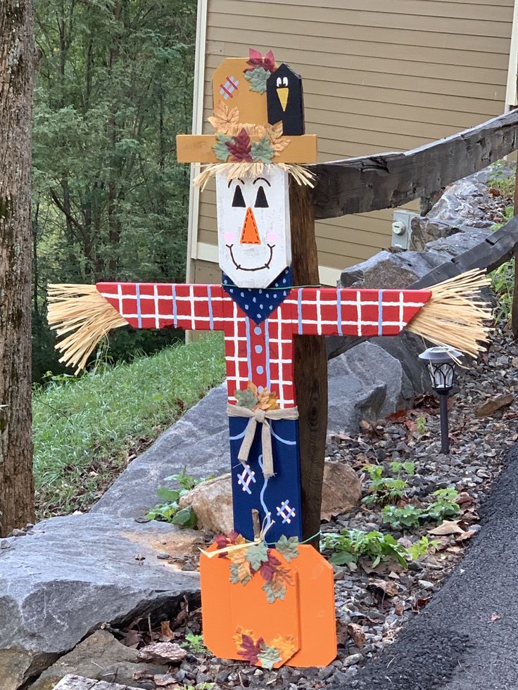 a scarecrow standing in front of a house with fall decorations on it's head