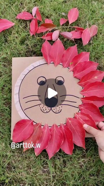 someone is holding up a paper cut out of a lion's head with leaves around it