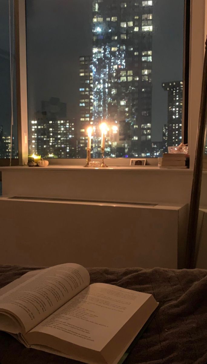 an open book sitting on top of a bed in front of a window at night