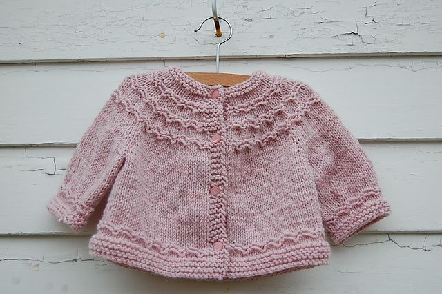 a pink knitted sweater hanging on a clothesline next to a white wooden wall