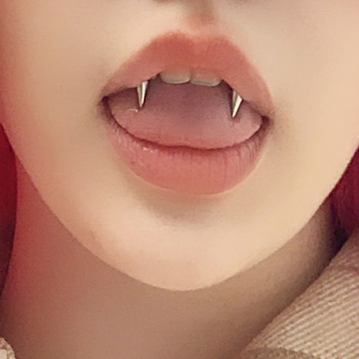 a woman with red hair and piercings on her teeth