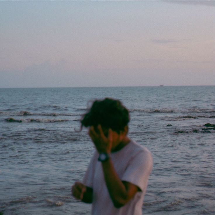 a man standing on top of a beach next to the ocean holding his head in his hands