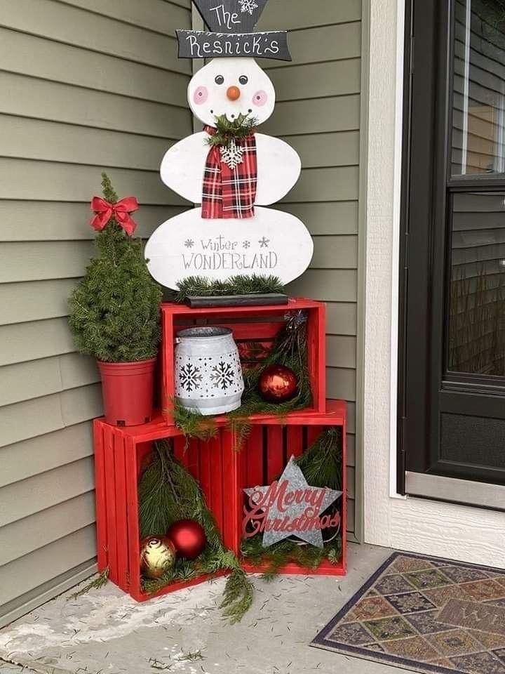 a snowman made out of crates sitting on the side of a house with christmas decorations