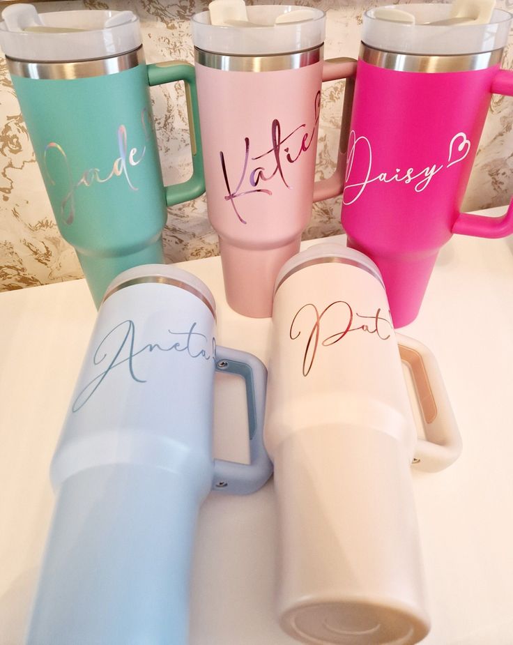 four different colored coffee mugs sitting on a counter next to each other with names