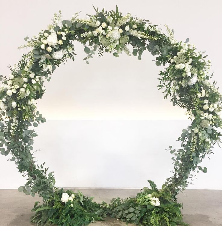 an arrangement of white flowers and greenery arranged in a circle on concrete flooring