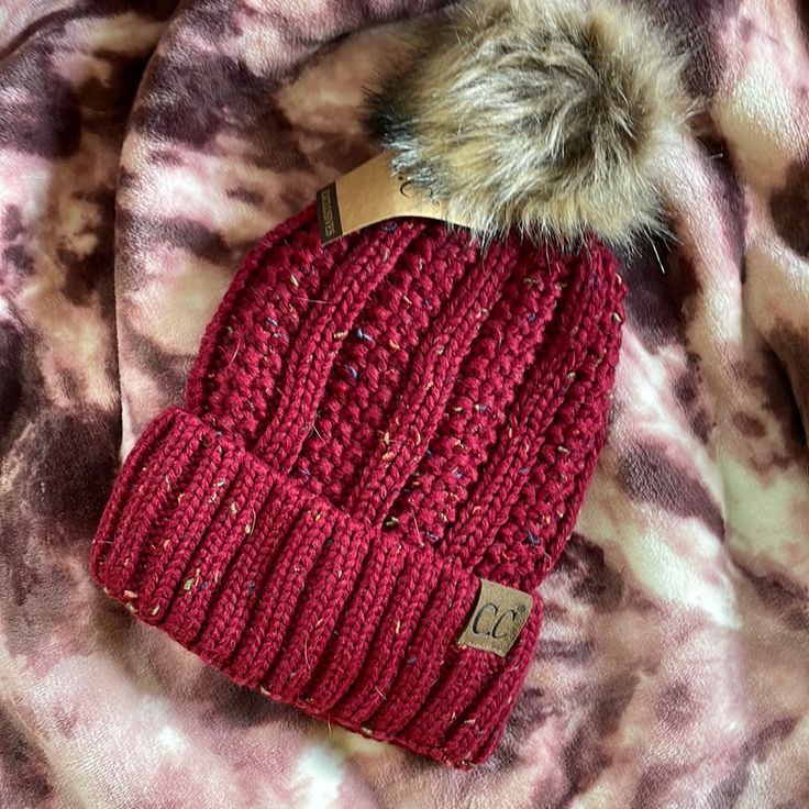 a red knit hat with a fur pom on it sitting on top of a blanket