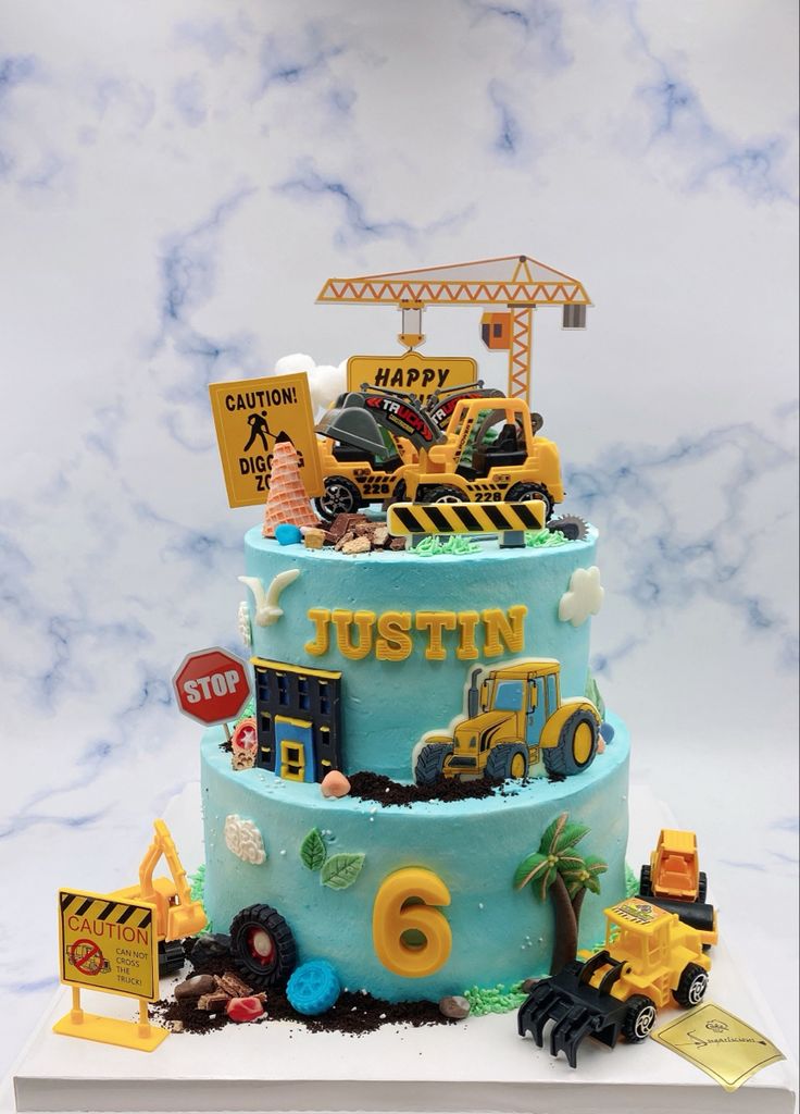 a three tiered cake with construction vehicles on top and blue frosting, sitting on a white surface