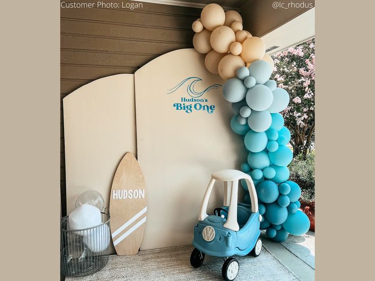 a blue car is parked in front of a surfboard and balloon arch that reads, welcome to the big one