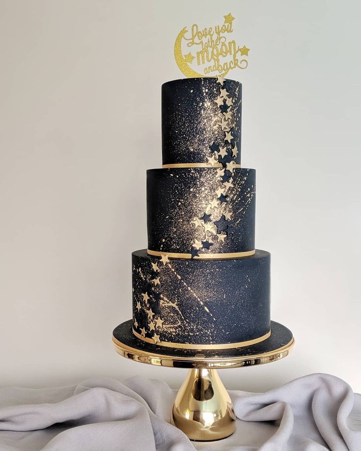 a three tiered black and gold wedding cake with stars on the top is sitting on a stand