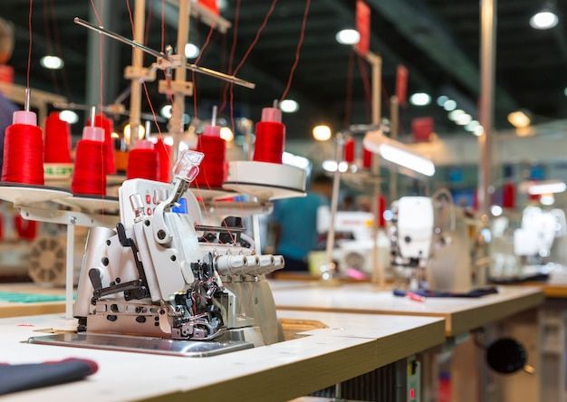 an industrial sewing machine with red thread on it's head in a room full of other machines