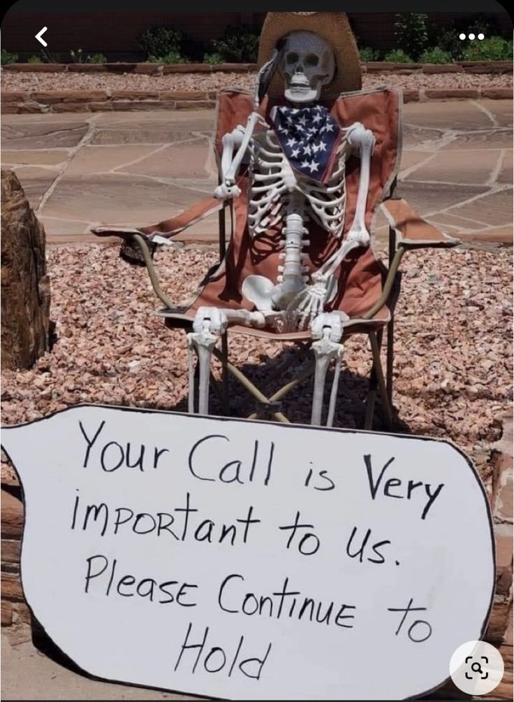 a skeleton sitting in a chair with a sign that says, your call is very important to us please continue to hold