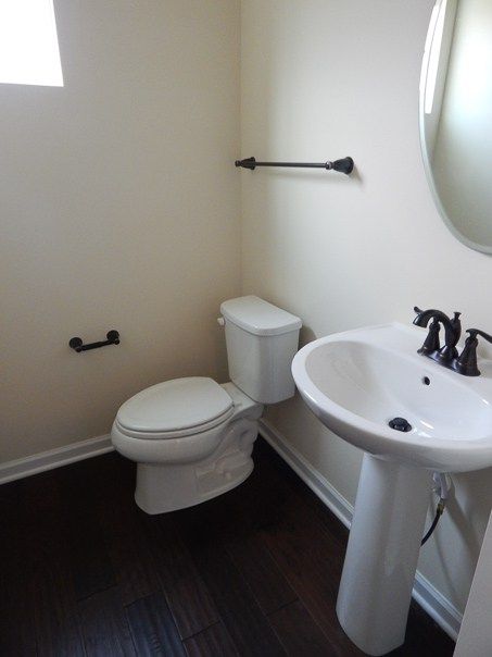 a white toilet sitting next to a sink in a bathroom under a window with dark wood floors