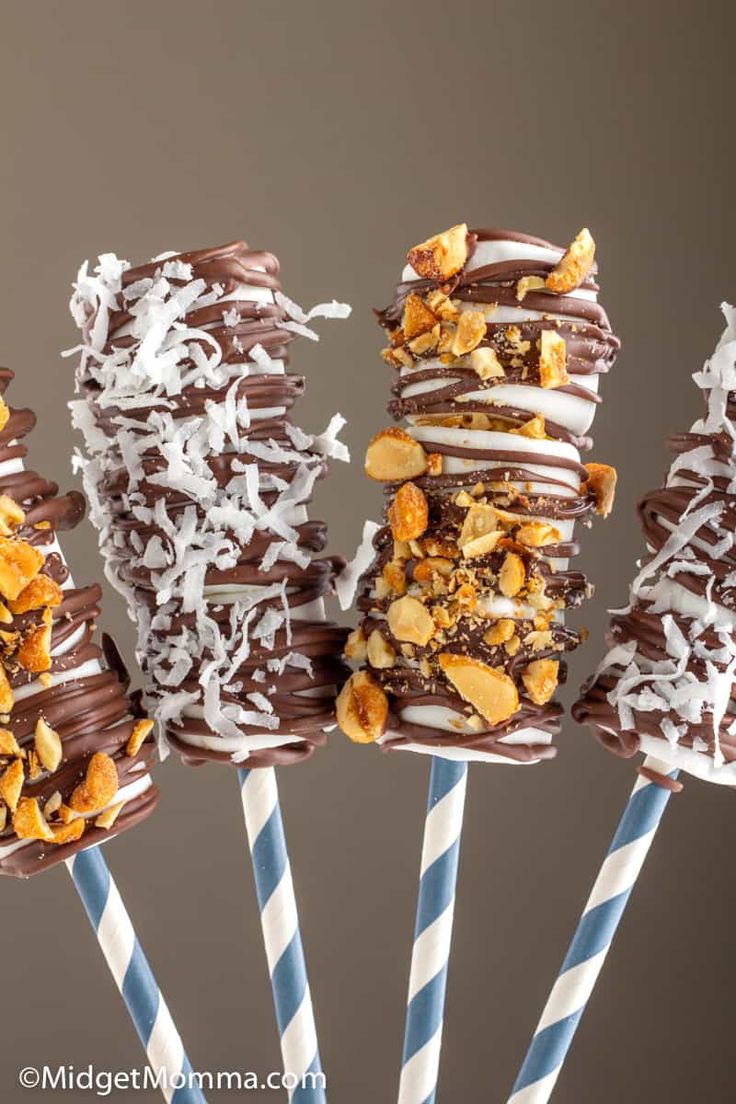 four chocolate covered donuts on top of blue and white striped straws with toppings