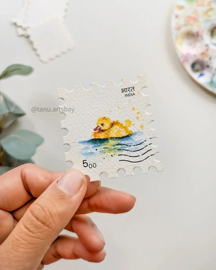 a person holding a rubber stamp with a ducky on it's back and watercolors in the background