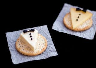 two crackers decorated with cheese and black bow ties