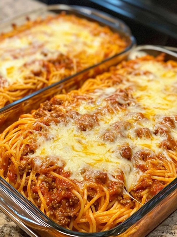 two glass casserole dishes filled with spaghetti and meat sauce on top of a granite counter