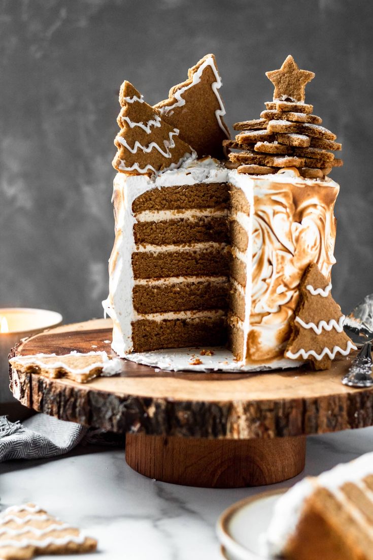 a slice of gingerbread cake with white frosting on a wooden platter next to some cookies