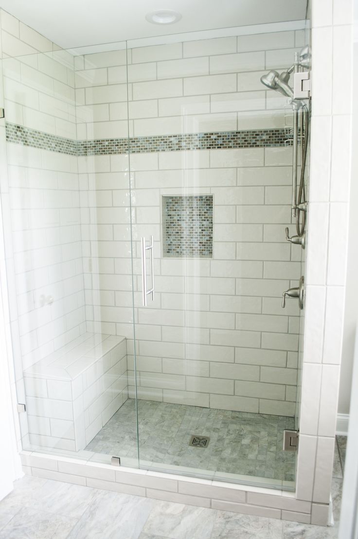 a walk in shower sitting next to a white tiled wall and floor with a glass door