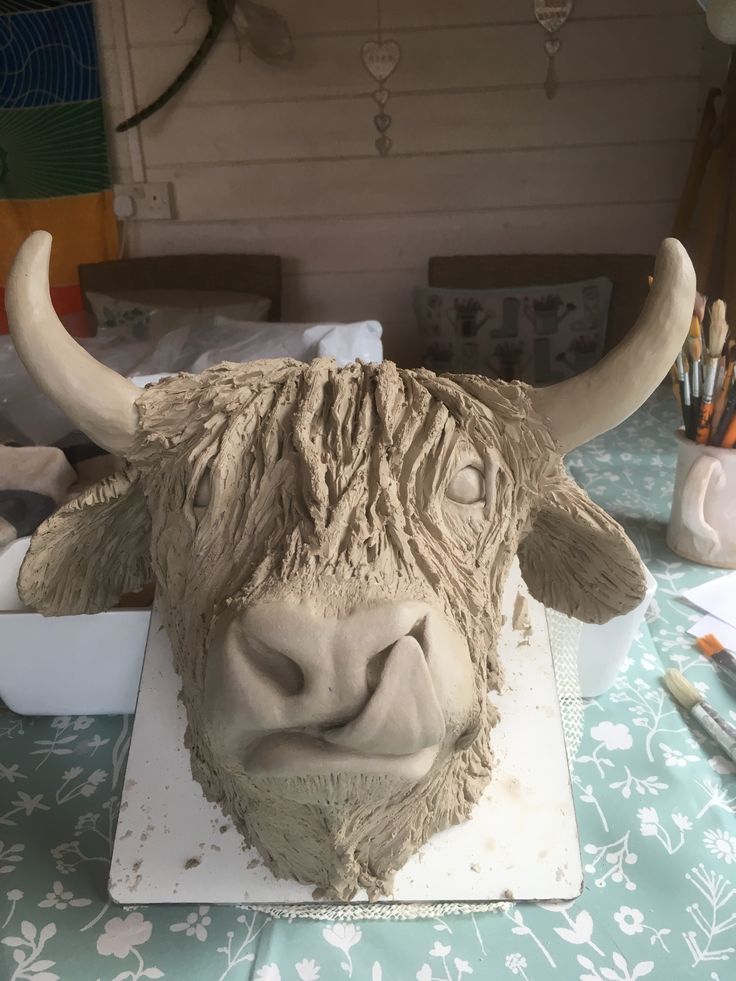 a clay sculpture of a bull's head on a table with paintbrushes