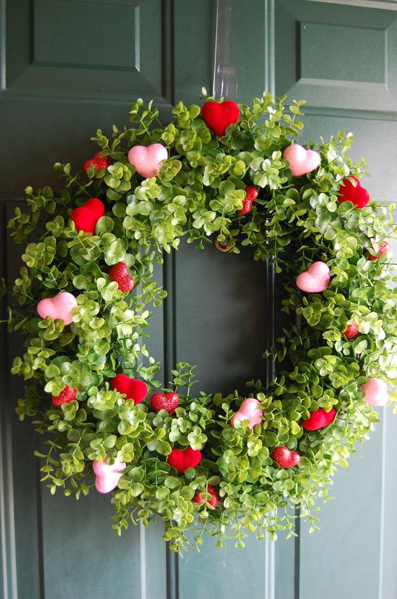 a wreath with hearts and greenery hanging on the front door for valentine's day