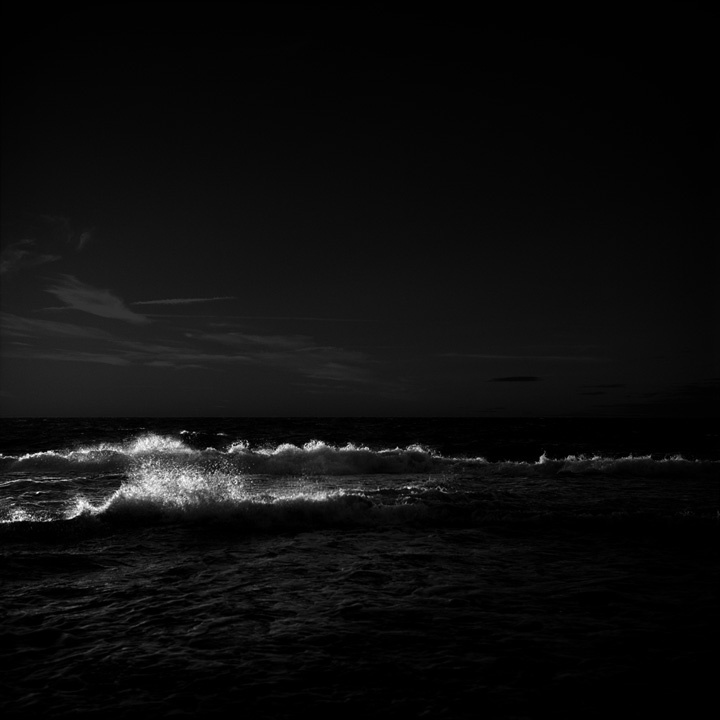 a black and white photo of waves in the ocean at night with a full moon