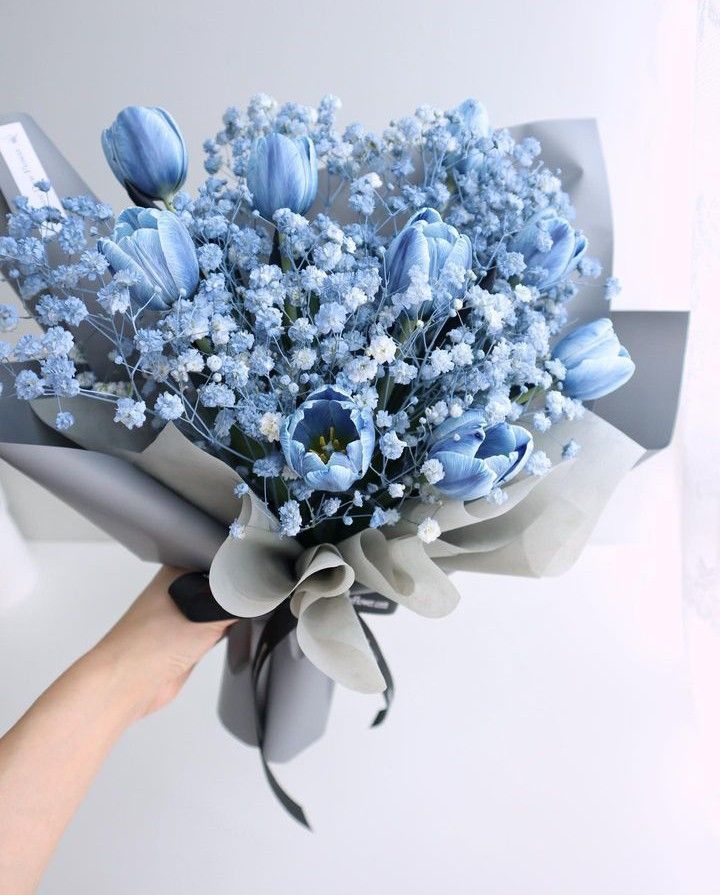 a bouquet of blue flowers being held by a person's hand on a white background