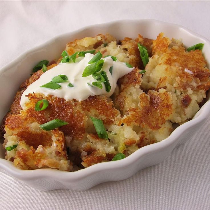 a white bowl filled with potatoes covered in sour cream and garnished with green onions