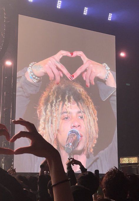 a man with dreadlocks holding his hands up in front of a large screen