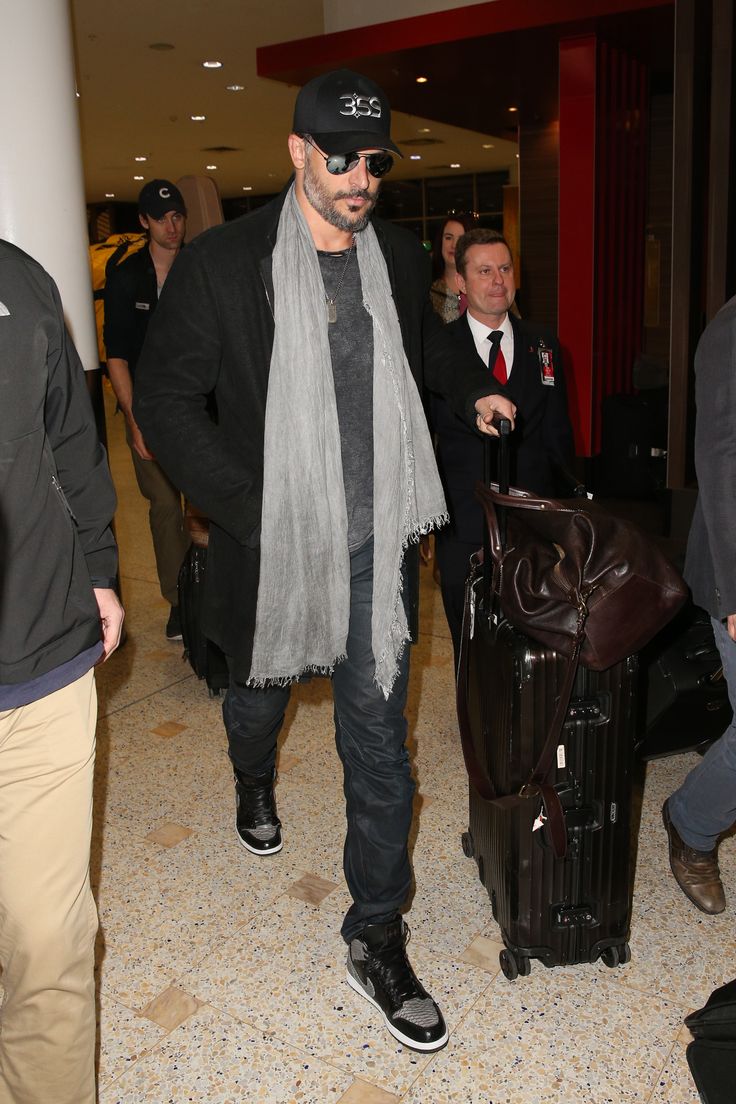 a man is walking through an airport with his luggage and scarf draped around his neck