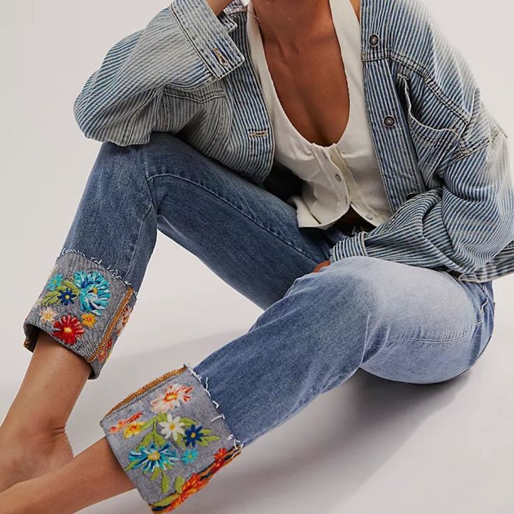 a woman sitting on the ground with her legs crossed wearing jeans and a jean jacket