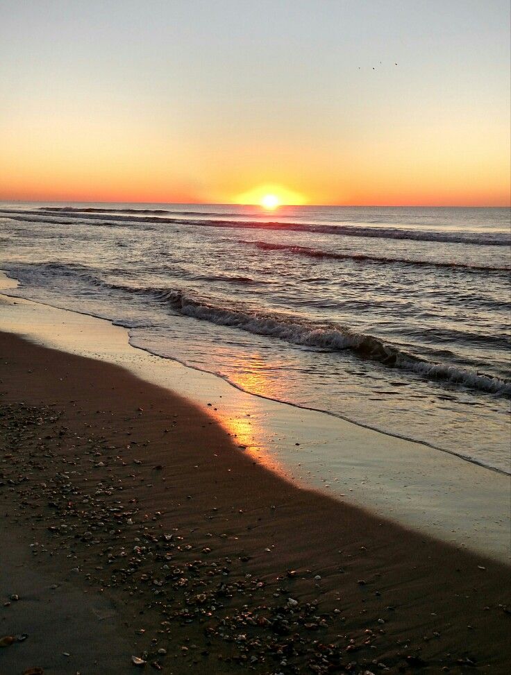 the sun is setting over the water at the beach