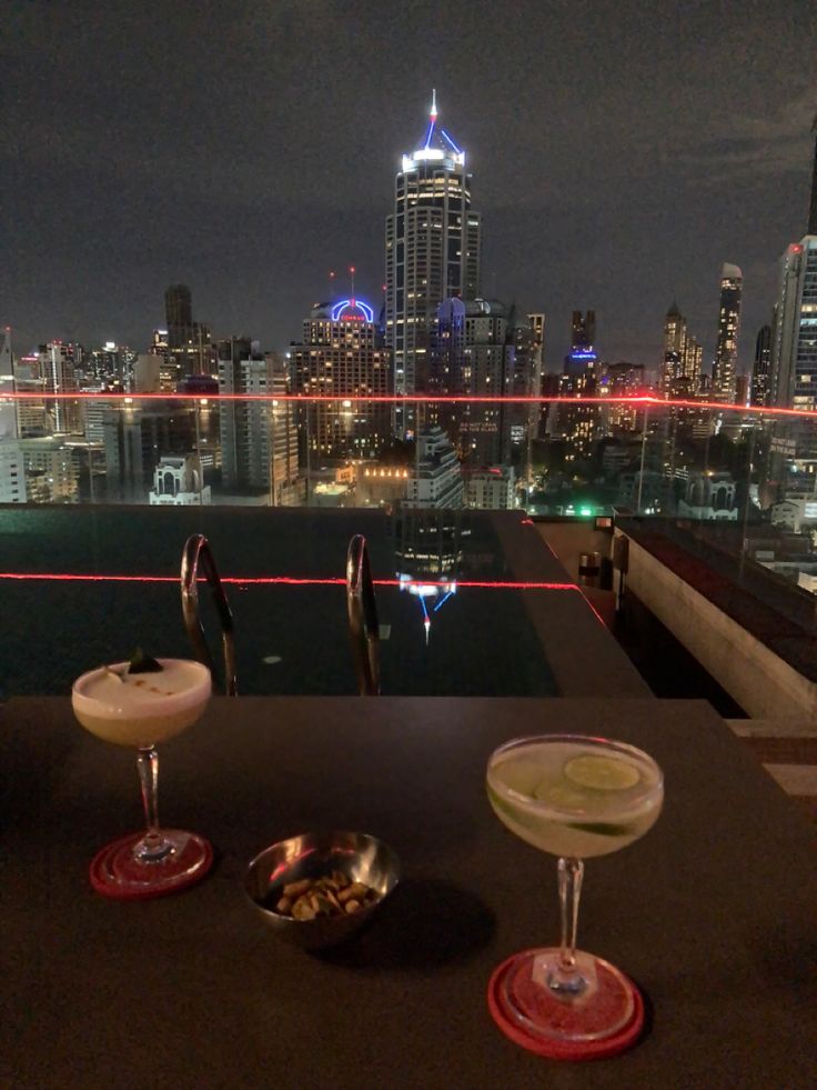 two drinks are sitting next to each other in front of a cityscape at night