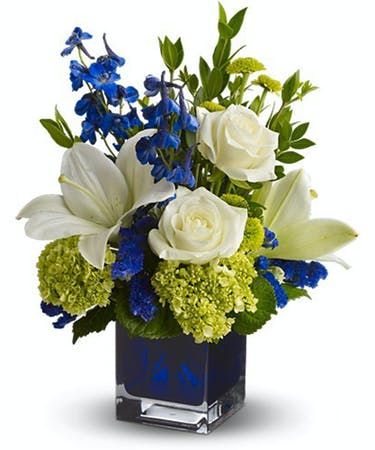 blue and white flowers in a square vase with greenery on the side, including roses