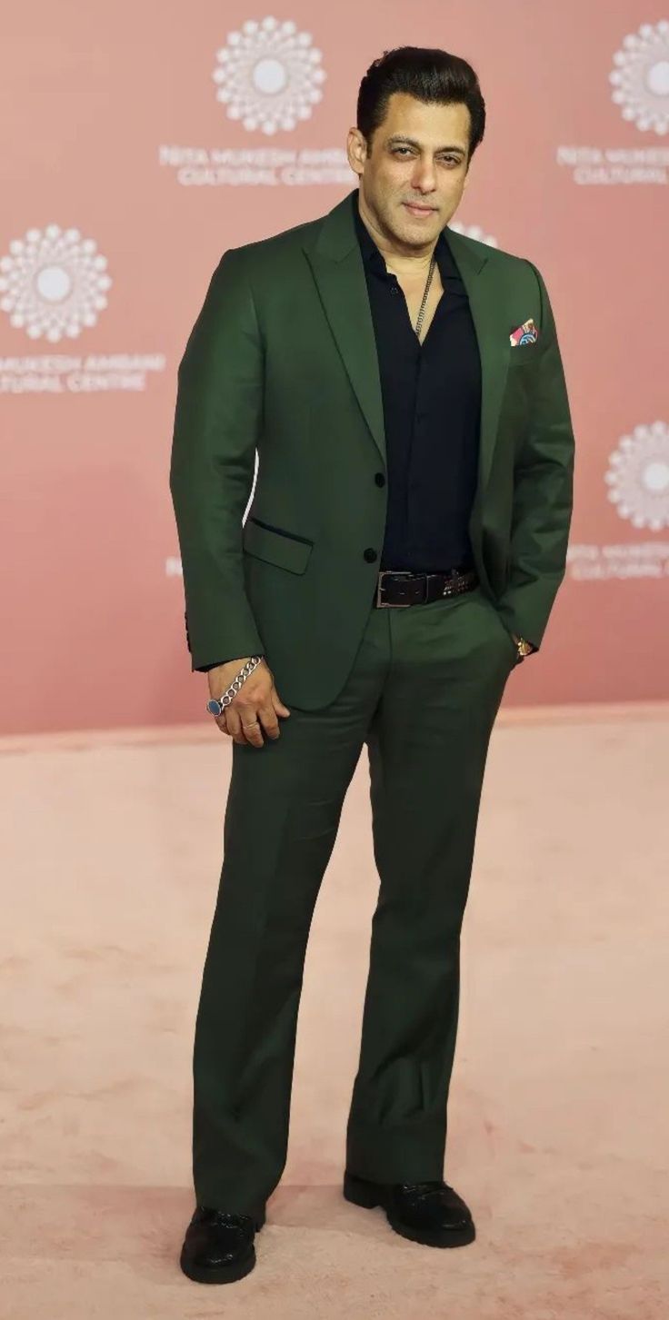 a man in a green suit and black shirt posing for the camera with his hands on his hips