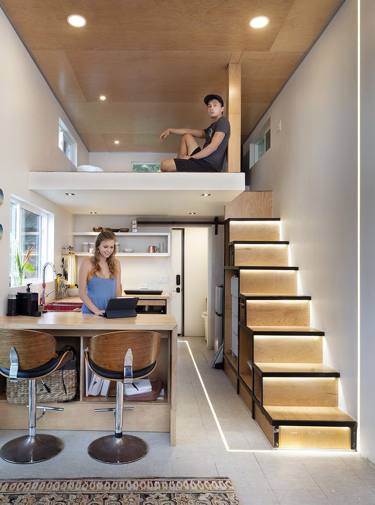 two people are sitting on the stairs in this small house with wood flooring and white walls