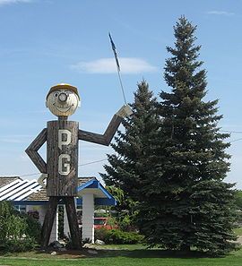 a large wooden figure holding a golf club next to a pine tree in front of a house