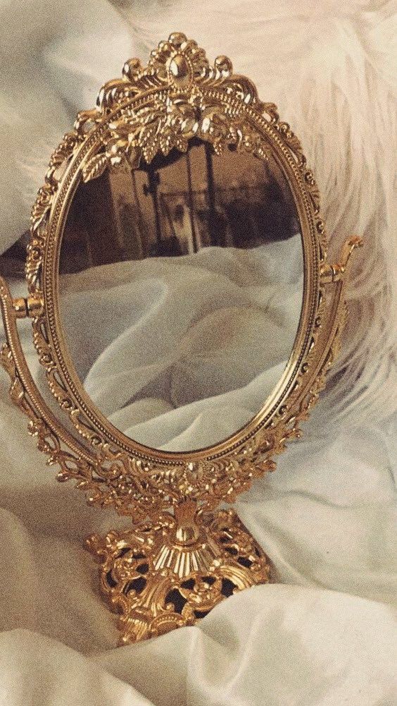 an ornate gold mirror sitting on top of a white bed next to a fluffy white blanket