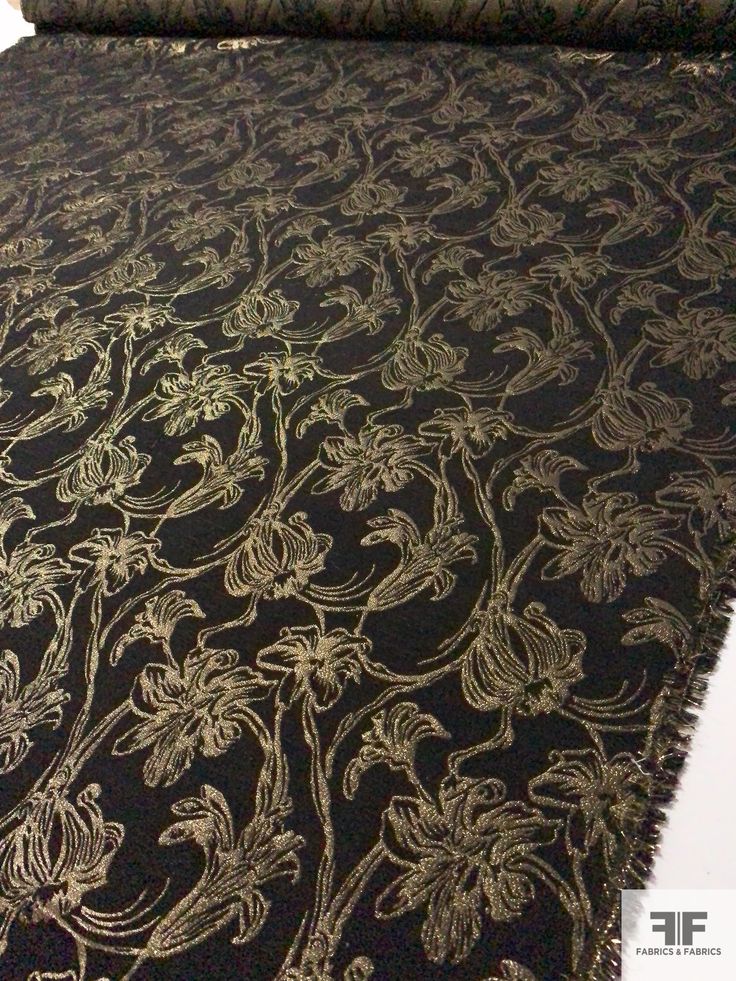 a black and gold table cloth with floral designs on it's edges, rolled up in front of a white wall