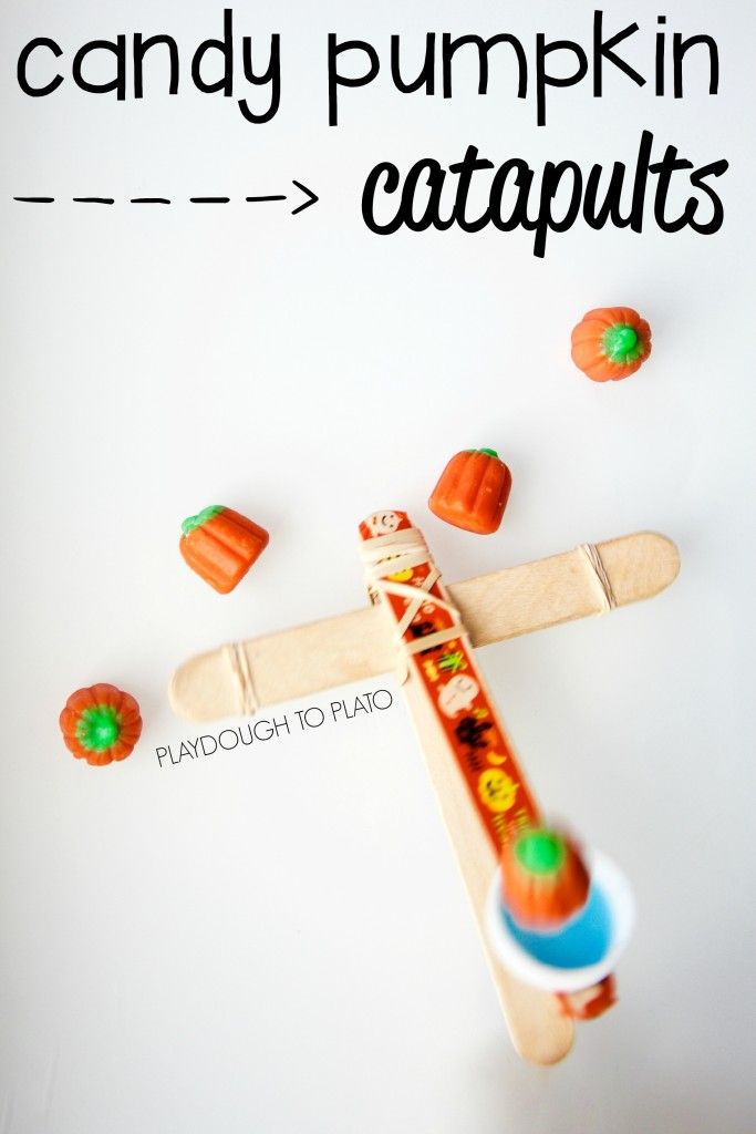 a wooden toy airplane with candy pumpkins on the ground next to it and text that reads, candy pumpkin catapults