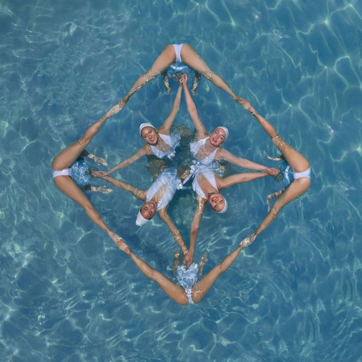 four people are floating in the water on their stomachs and arms around each other