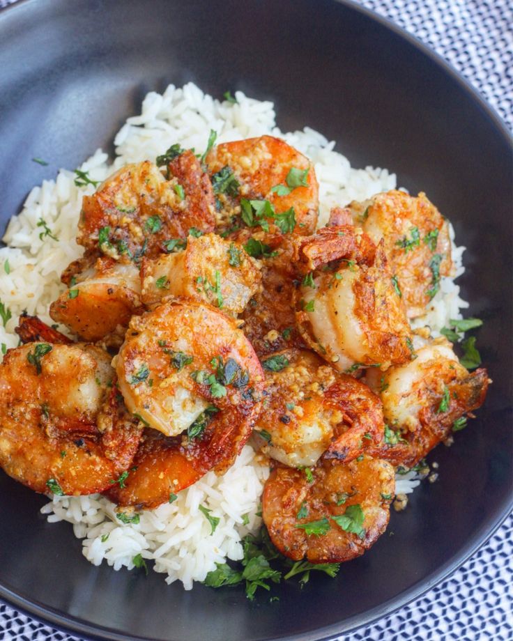 a black plate topped with rice and shrimp on top of a blue checkered table cloth