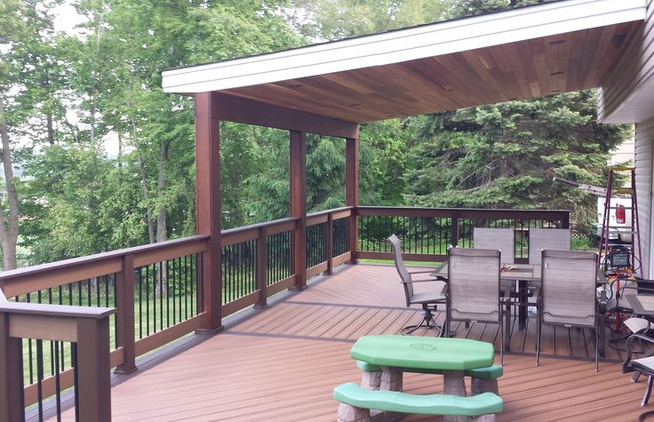 a wooden deck with chairs and tables on it, surrounded by trees in the background